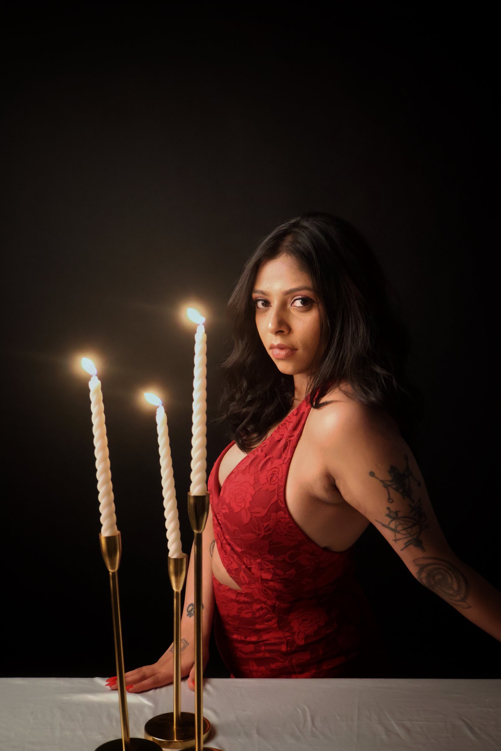 Mrunalini in a deep red dress beside lit candles, one warm light source against darkness