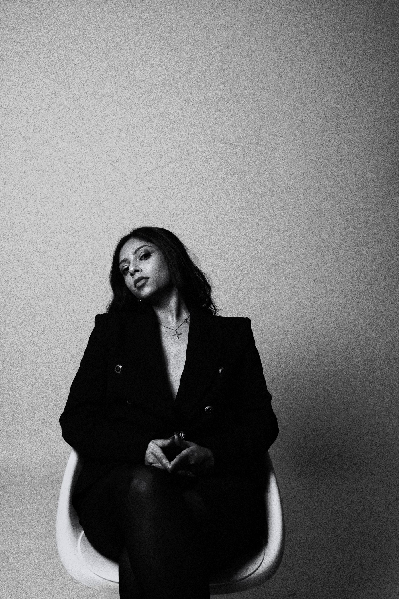 Mrunalini seated in a black blazer, black and white portrait, head tilted, gazing at the camera